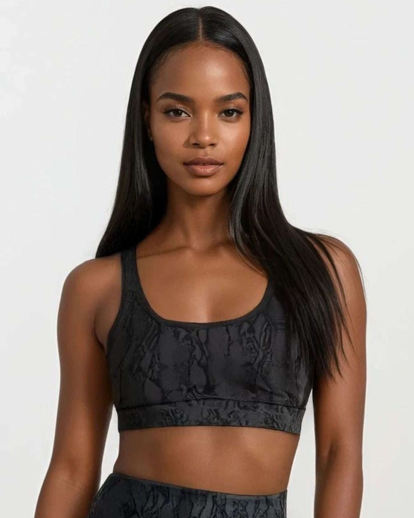 Woman wearing a black patterned sports bra and leggings on a white background