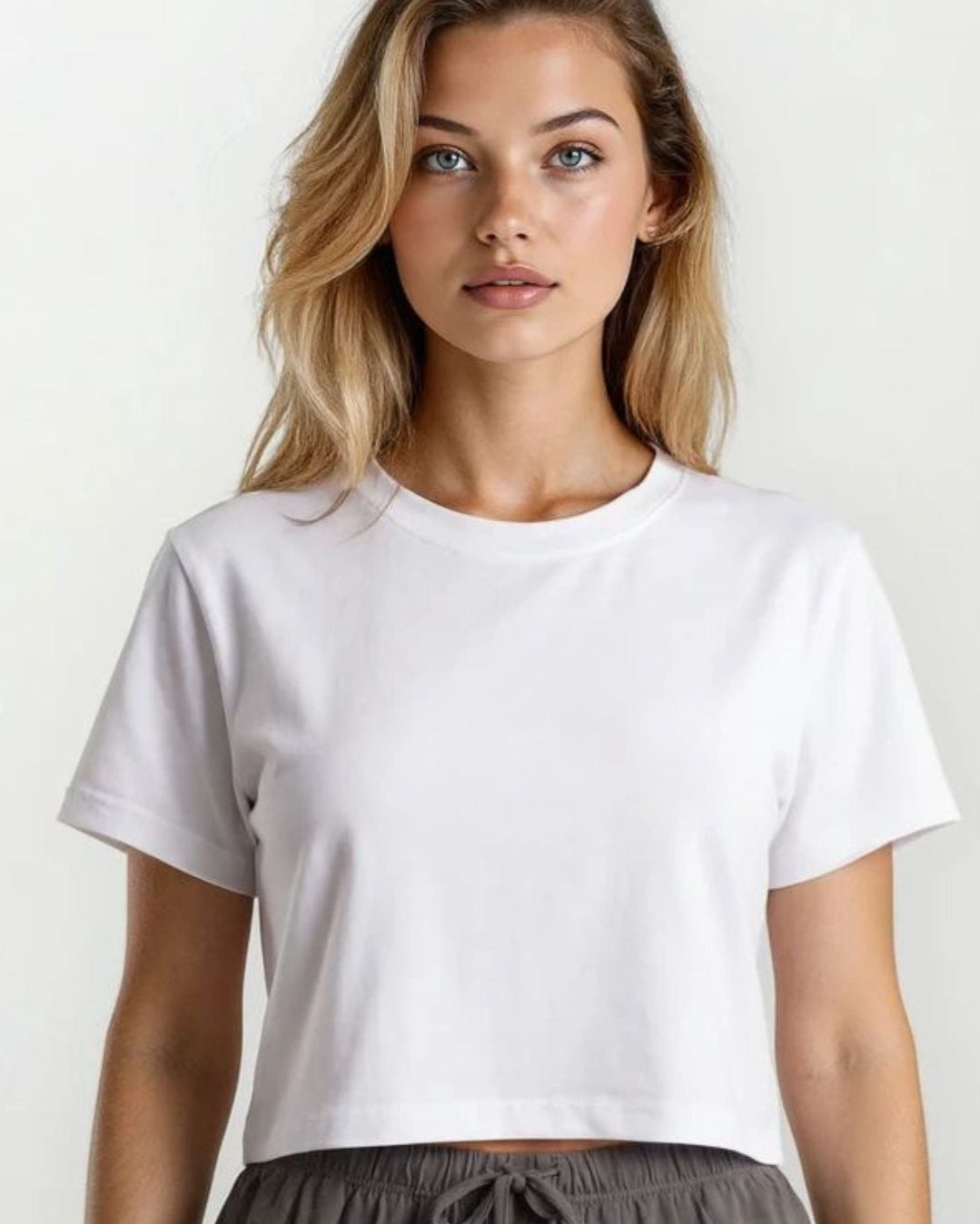 Woman wearing a white t-shirt and gray pants against a plain background