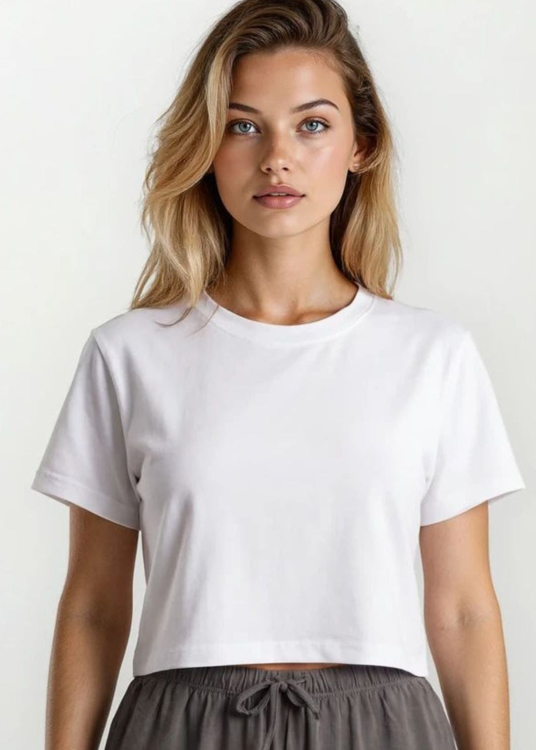 Woman wearing a white t-shirt and gray pants against a plain background