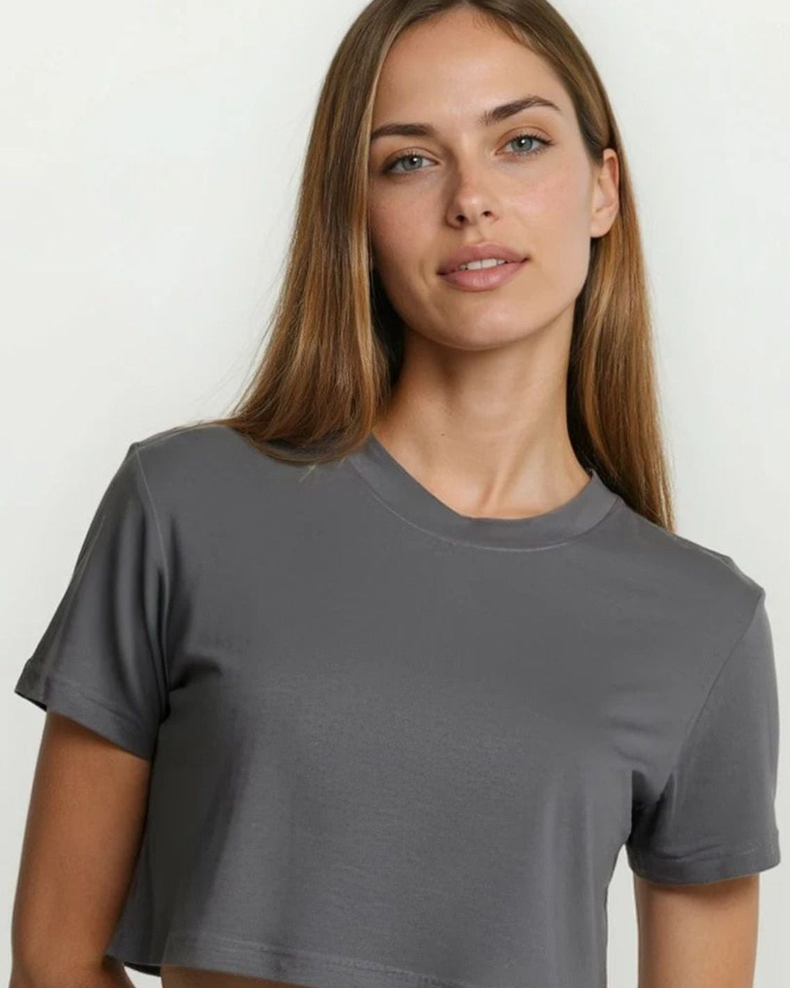 Woman wearing a gray crop top and gray pants against a white background