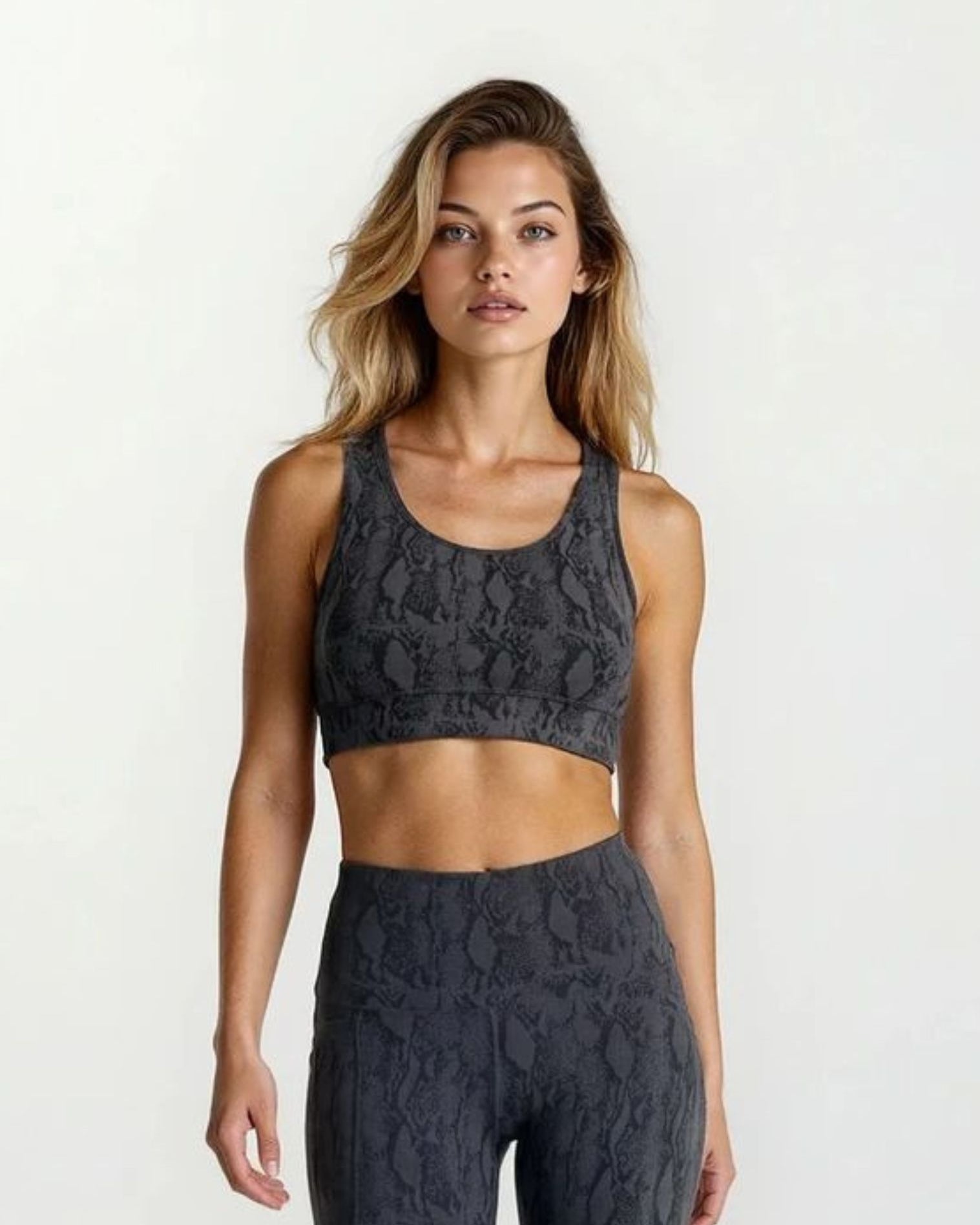 Woman wearing a dark gray snake skin design bamboo high impact sports bra and leggings set on a white background
