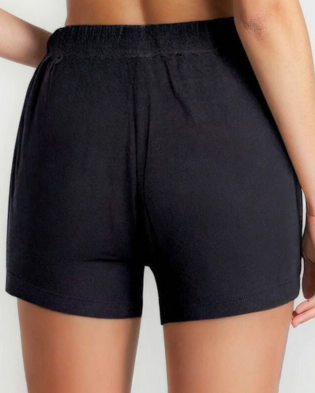 Person wearing black athletic shorts and a dark sports bra on a light background