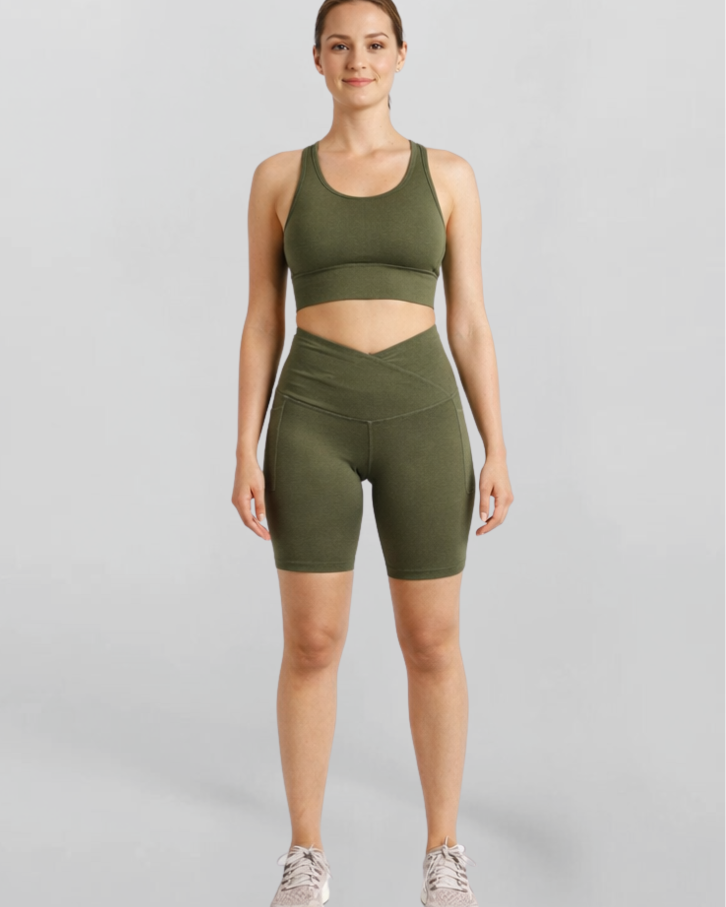 Woman wearing an olive green khaki bike shorts and sports bra athletic outfit on a gray background