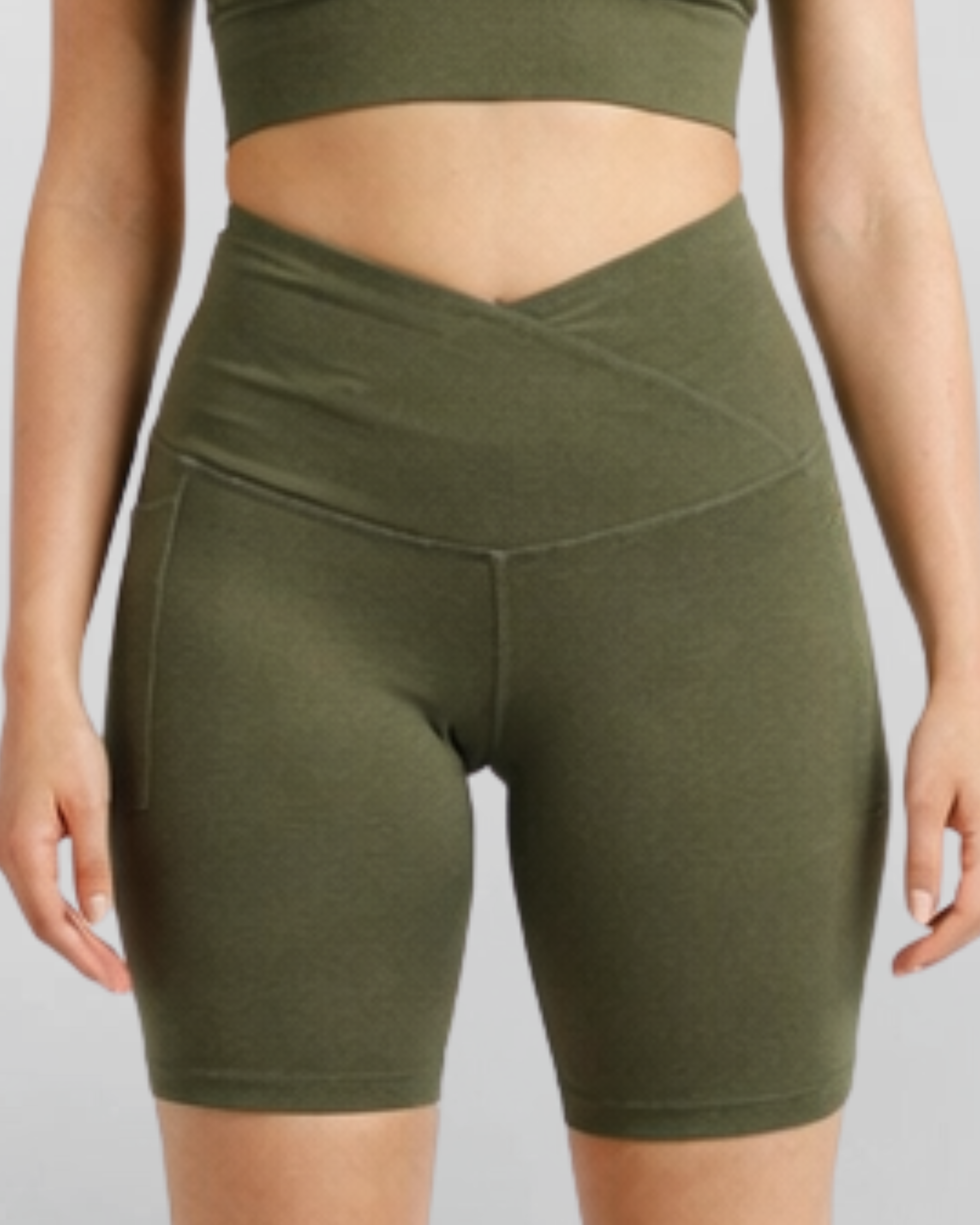 Woman wearing olive green athletic shorts Motion Khaki Bike Shorts Cross V Waist Bamboo soft and moisture wicking gym yoga pilates short sustainable skin friendly on a plain background