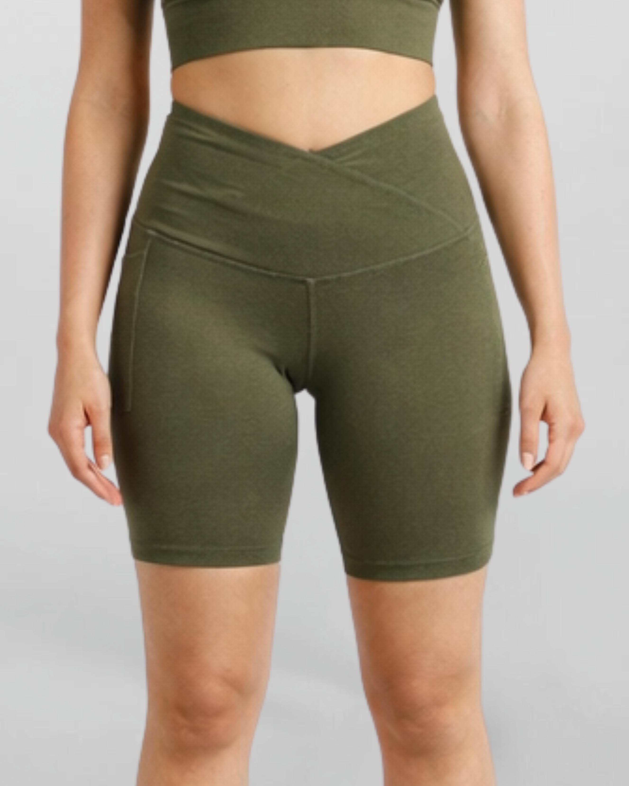 Woman wearing olive green athletic shorts Motion Khaki Bike Shorts Cross V Waist Bamboo soft and moisture wicking gym yoga pilates short sustainable skin friendly on a plain background