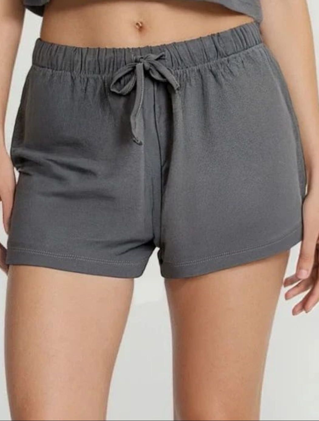 Person wearing gray shorts and a cropped top on a white background