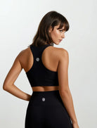 Woman wearing a racerback black high impact bamboo sports bra and leggings on a white background