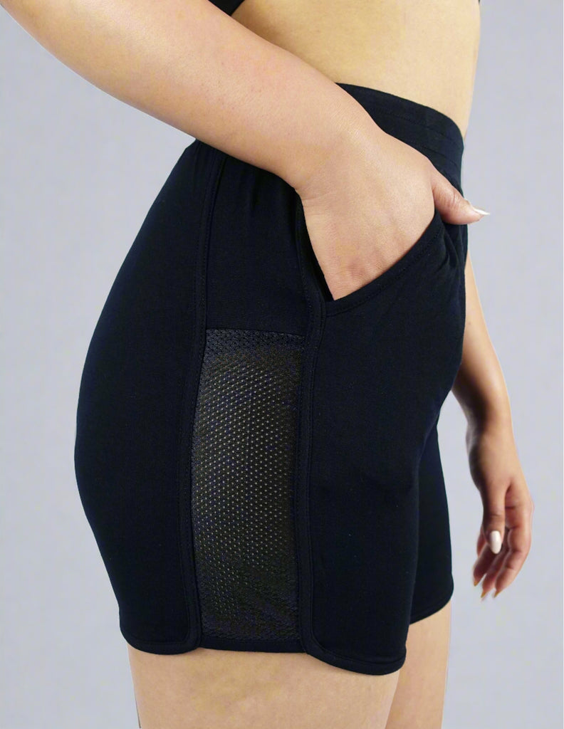 Side view of women's mid length shorts with mesh fabrication on sides and pocket 