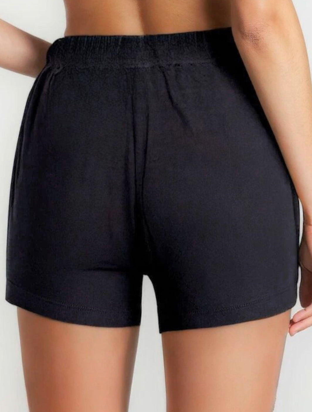 Person wearing black athletic shorts and a dark sports bra on a light background