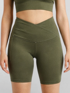 Woman wearing olive green athletic shorts Motion Khaki Bike Shorts Cross V Waist Bamboo soft and moisture wicking gym yoga pilates short sustainable skin friendly on a plain background