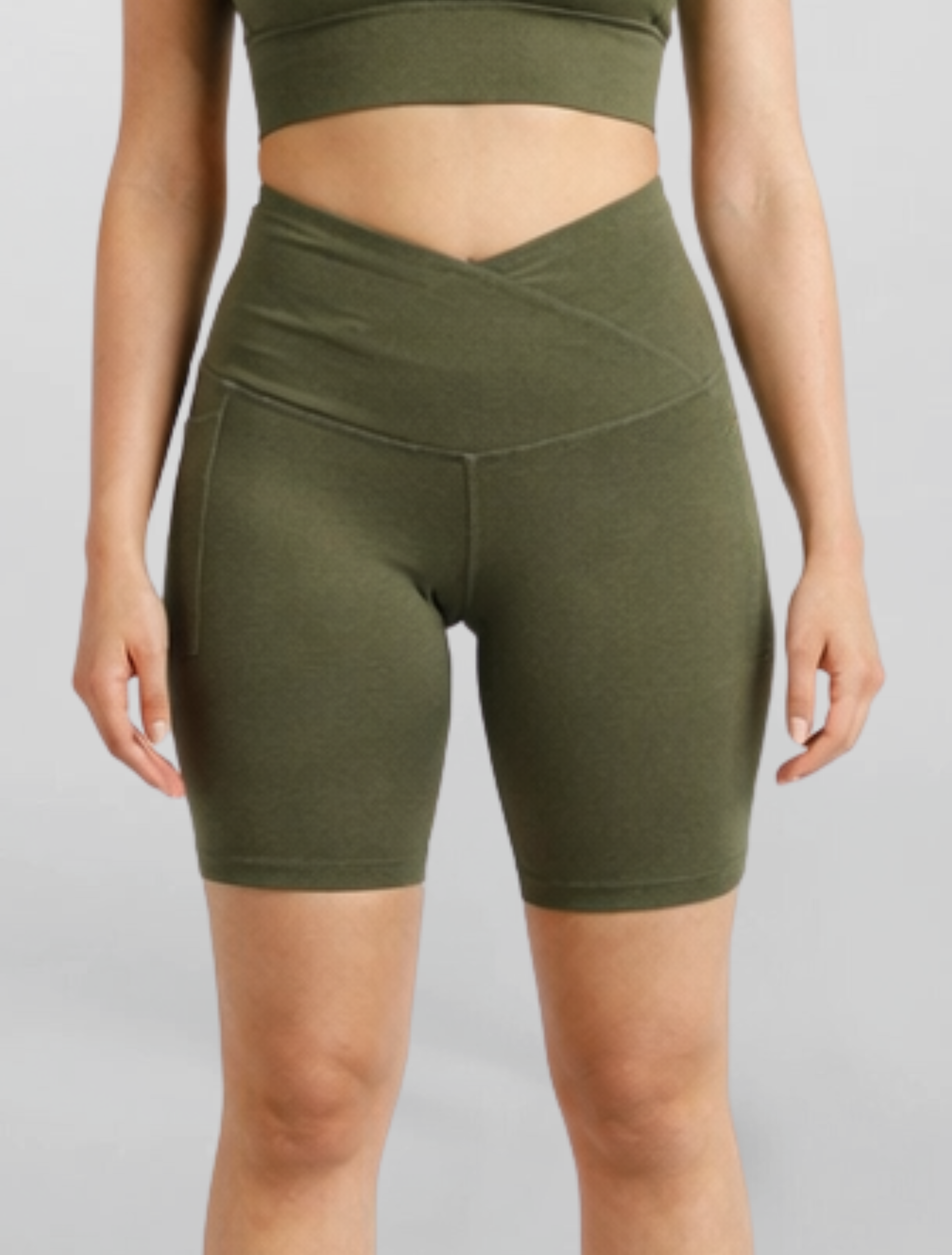 Woman wearing olive green athletic shorts Motion Khaki Bike Shorts Cross V Waist Bamboo soft and moisture wicking gym yoga pilates short sustainable skin friendly on a plain background