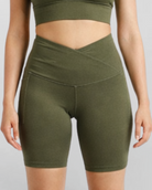 Woman wearing olive green athletic shorts Motion Khaki Bike Shorts Cross V Waist Bamboo soft and moisture wicking gym yoga pilates short sustainable skin friendly on a plain background