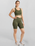 Woman wearing an olive green athletic outfit Motion Khaki Cross V Waist Bike Shorts Bamboo soft and moisture wicking performance gym yoga pilates short on a gray background